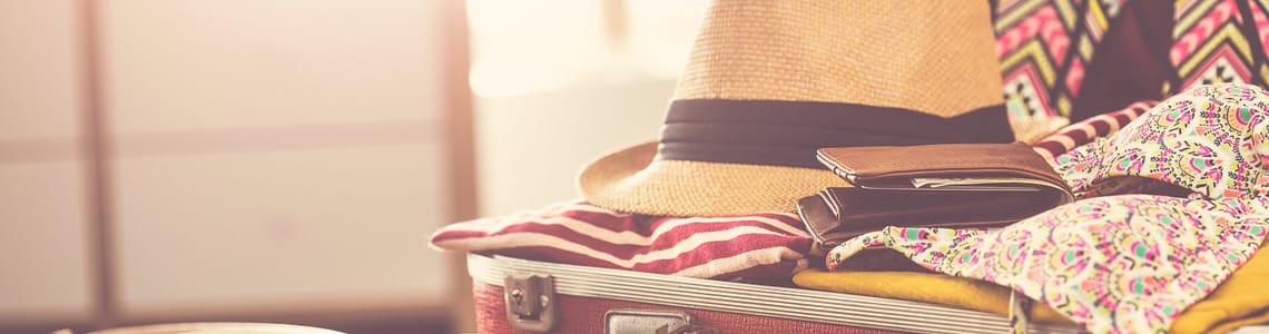 A neatly arranged suitcase with essentials for a yacht trip, including swimwear, a wide-brimmed hat, sunglasses, and lightweight clothing, all set against a nautical-themed backdrop.