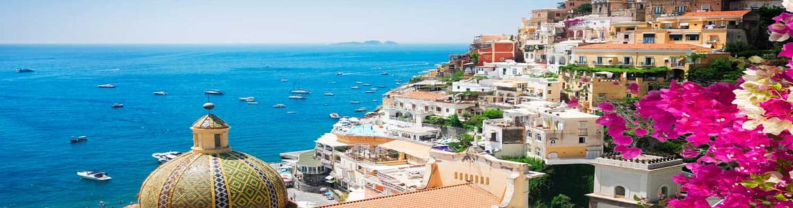 Scenic view of Positano, Italy with colorful hillside buildings, vibrant flowers, and boats on the turquoise Mediterranean Sea.