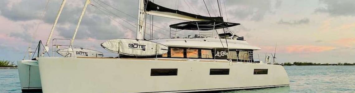 Luxury catamaran yacht moored on turquoise water at sunset with vibrant skies.