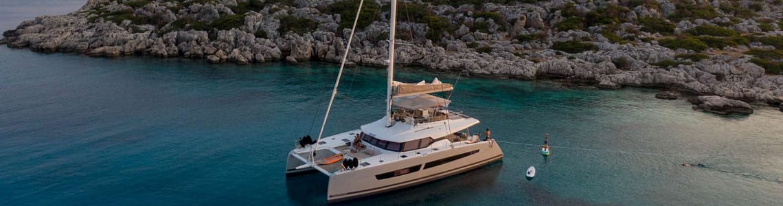 Luxury catamaran anchored in a serene bay with rocky hills and clear turquoise water, ideal for a peaceful sailing getaway.