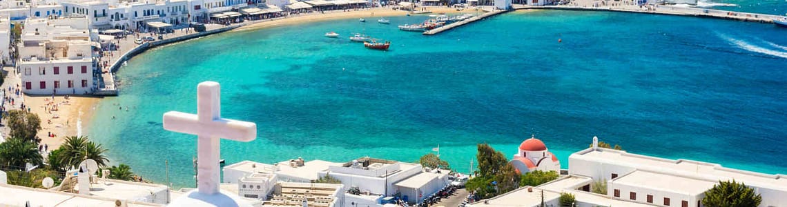 Panoramic view of Mykonos town with vibrant blue sea, white buildings, and church rooftops in Greece.