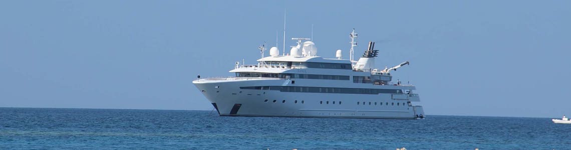 Luxury yacht sailing on a clear blue ocean near a sandy beach, under a bright blue sky