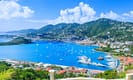 Panoramic view of tropical harbor with sailboats and lush green hills in the Caribbean, under a clear blue sky.