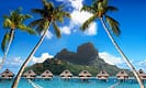 Tropical island paradise with palm trees, overwater bungalows, and a hammock on a sandy beach against a mountainous backdrop.
