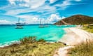 Tropical beach with turquoise waters, sailboats, and a hilly landscape in the British Virgin Islands.