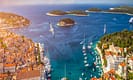 Scenic aerial view of Hvar, Croatia, featuring vibrant orange rooftops, clear blue Adriatic Sea, sailboats, yachts, and lush green islands.