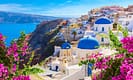 Scenic view of Santorini, Greece with iconic white buildings and blue domes overlooking the Aegean Sea, surrounded by vibrant pink flowers.