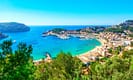 Scenic view of Port de Sóller in Mallorca with turquoise waters, vibrant coastal town, lush green hills, and clear blue sky.
