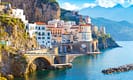 Scenic view of Amalfi Coast village with colorful houses and arched bridge over clear blue sea, mountain backdrop