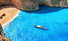 Navagio Beach in Zakynthos, Greece with clear turquoise water, a shipwreck on the sandy shore, and a boat floating nearby.