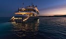 Luxury yacht Serenity illuminated at dusk, cruising on serene waters with a beautiful sunset in the background.