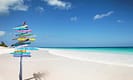 Tropical beach with colorful directional signpost under clear blue sky.