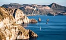 Scenic view of rocky coastline and calm sea with sailboats near the Aeolian Islands, Italy, showcasing natural beauty and serene landscape.