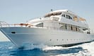 Luxury white yacht cruising on open sea with clear blue skies and waves.