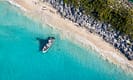 Aerial view of a boat anchored near a pristine sandy beach with clear turquoise water and lush greenery on a sunny day.