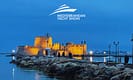 Night view of a historic fortress illuminated along a rocky shoreline during the Mediterranean Yacht Show showcasing vibrant coastal scenery and maritime heritage.