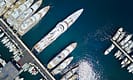 Aerial view of luxury yachts docked in a marina with shimmering water reflections.
