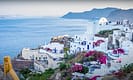 Scenic view of Santorini coastline with whitewashed buildings and vibrant bougainvillea, overlooking the Aegean Sea and distant islands.