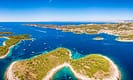 Aerial view of Hvar Islands in Croatia, showcasing turquoise waters, lush greenery, and numerous sailboats under a clear blue sky.
