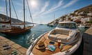 Wide-angle view of a Greek island marina with luxury motor yacht, classic sailboat, and modern catamaran docked. Sunlight highlights teak decks, chrome railings, and waterfront accessories, ideal for comparing yacht options for a memorable Greek adventure.