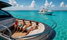 Two luxury yachts anchored in turquoise Bahamian waters; one private yacht with friends relaxing on deck, another group yacht nearby with water toys and families enjoying the sun. Crystal-clear water, island backdrop, and bright tropical sky create a vibrant, inviting scene.