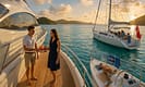 Two luxury yachts anchored in a turquoise bay at golden hour; one features a uniformed crew serving guests, the other shows a barefoot family relaxing. Lush green islets, sunlit decks, and nautical details highlight the contrast between crewed and bareboat yacht charters in the British Virgin Islands.
