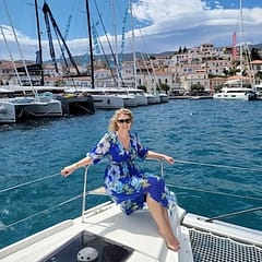 Woman enjoying a sunny day on a yacht in a marina with sailboats and a picturesque coastal town in the background.