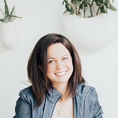 Smiling woman in denim jacket with indoor plants in background, bright and minimalistic setting