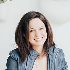 Smiling woman in denim jacket with indoor plants in background, bright and minimalistic setting