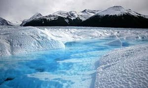 Majestic glacier landscape with icy blue water and snow-covered mountains in the background, showcasing natural beauty and climate change effects.