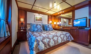 Luxurious yacht bedroom interior with a large bed, elegant bedding, ambient lighting, wood paneling, and a flat-screen TV.