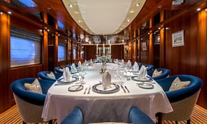 Luxurious yacht dining room with elegantly set table, plush blue chairs, and polished wood paneling, creating an upscale and sophisticated atmosphere.