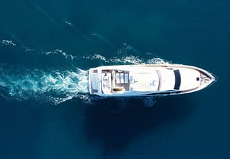 Aerial view of a luxury yacht cruising through clear blue ocean waters with visible wake trail.