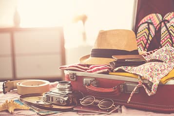 A neatly arranged suitcase with essentials for a yacht trip, including swimwear, a wide-brimmed hat, sunglasses, and lightweight clothing, all set against a nautical-themed backdrop.