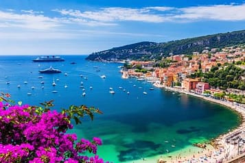 Scenic view of Villefranche-sur-Mer coastline with vibrant Mediterranean colors, yachts in the bay, and vivid purple bougainvillea in the foreground.