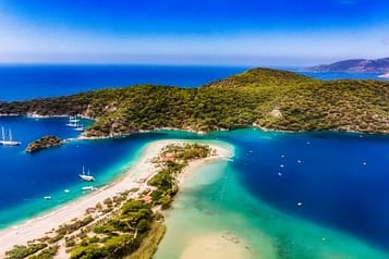 Aerial view of Ölüdeniz beach and stunning turquoise lagoon, surrounded by lush green hills and sailboats, in Turkey's Mediterranean coast.
