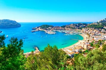 Scenic view of Port de Sóller in Mallorca with turquoise waters, vibrant coastal town, lush green hills, and clear blue sky.