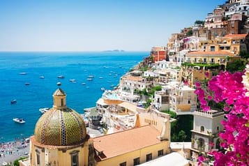 Scenic view of Positano on the Amalfi Coast, featuring colorful cliffside buildings, vibrant bougainvillea, and boats dotting the turquoise sea.