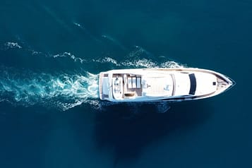 Aerial view of a luxury yacht cruising through clear blue ocean waters with visible wake trail.