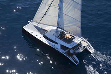 Luxury sailing catamaran cruising in clear blue ocean waters with sun reflecting on the surface, showcasing elegant design and spacious deck.