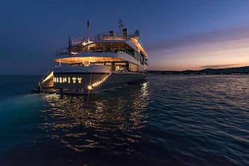 Luxury yacht Serenity illuminated at dusk, cruising on serene waters with a beautiful sunset in the background.