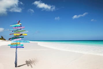 Tropical beach with colorful directional signpost under clear blue sky.