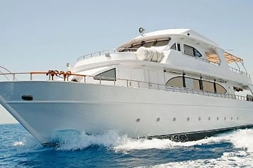 Luxury white yacht cruising on open sea with clear blue skies and waves.