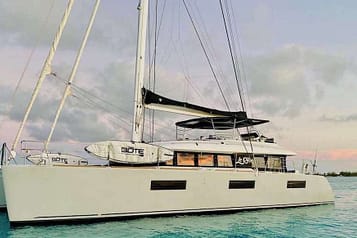 Catamaran yacht on calm ocean water at sunset with paddleboards, featuring a sleek design and modern sails.