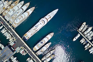Aerial view of luxury yachts docked in a marina with shimmering water reflections.