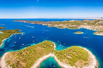 Aerial view of Hvar Islands in Croatia, showcasing turquoise waters, lush greenery, and numerous sailboats under a clear blue sky.