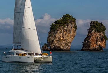 Sailboat cruising near limestone rock formations in Phang Nga Bay, Thailand, under clear skies.
