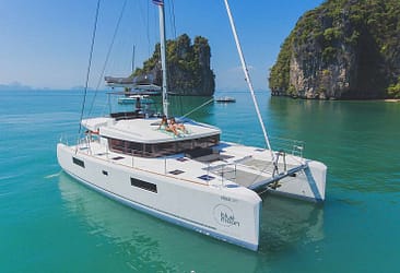 Luxury catamaran sailing in turquoise waters near lush limestone cliffs in a tropical paradise.
