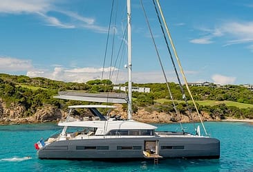 Luxury catamaran yacht anchored near a scenic coastline with clear blue water and greenery in the background.