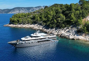 Luxury yacht anchored near a scenic coastline with lush greenery and clear blue waters.